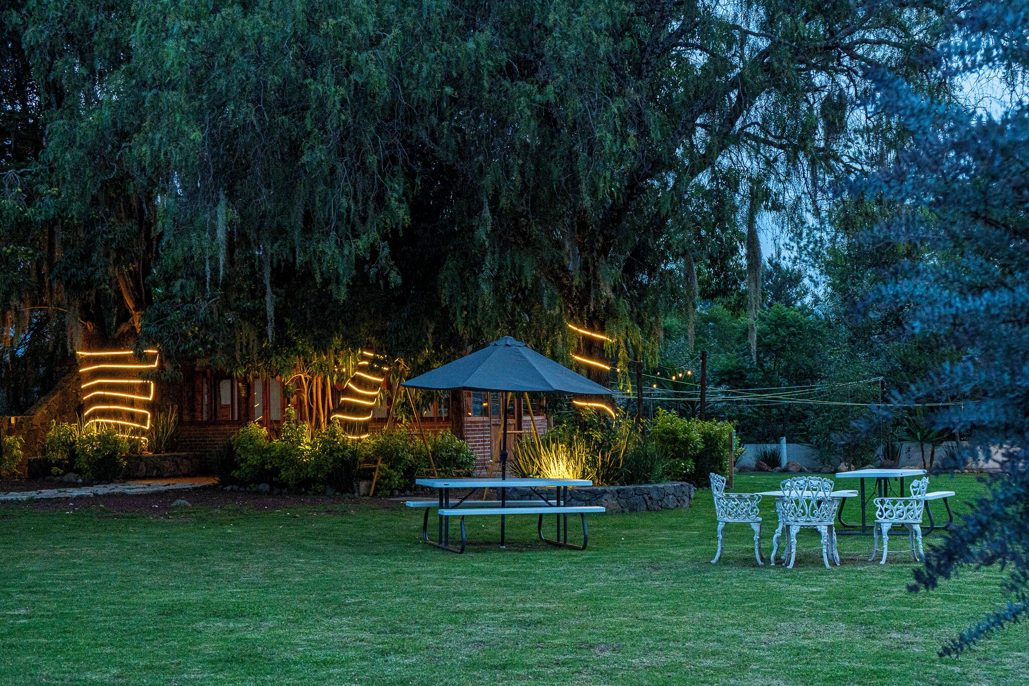 Un área de picnic con una mesa y sillas, un pabellón y un edificio con luces iluminadas.