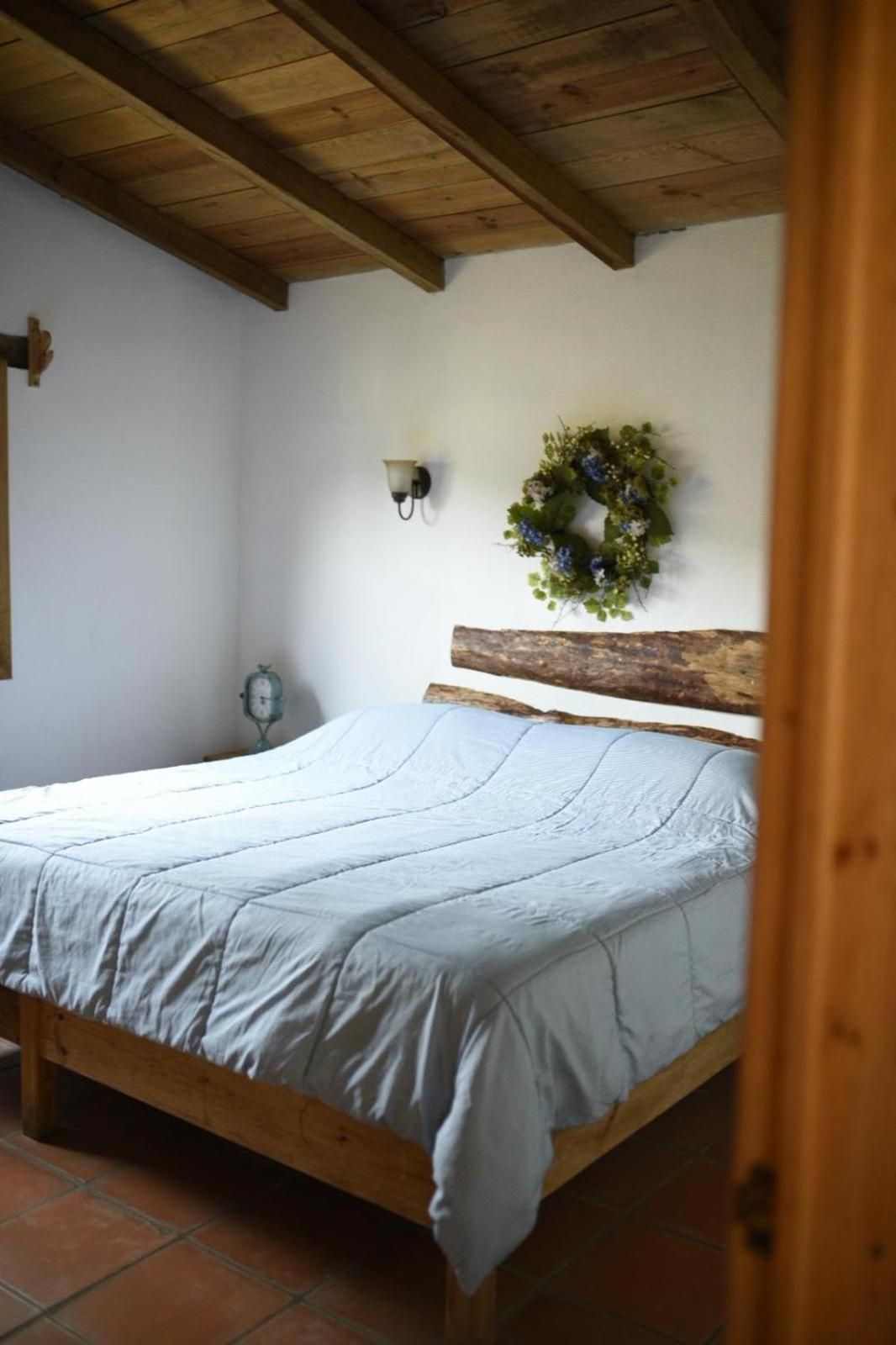 A bedroom with a wooden bed frame, a headboard, a wall-mounted light fixture, and a wall clock.