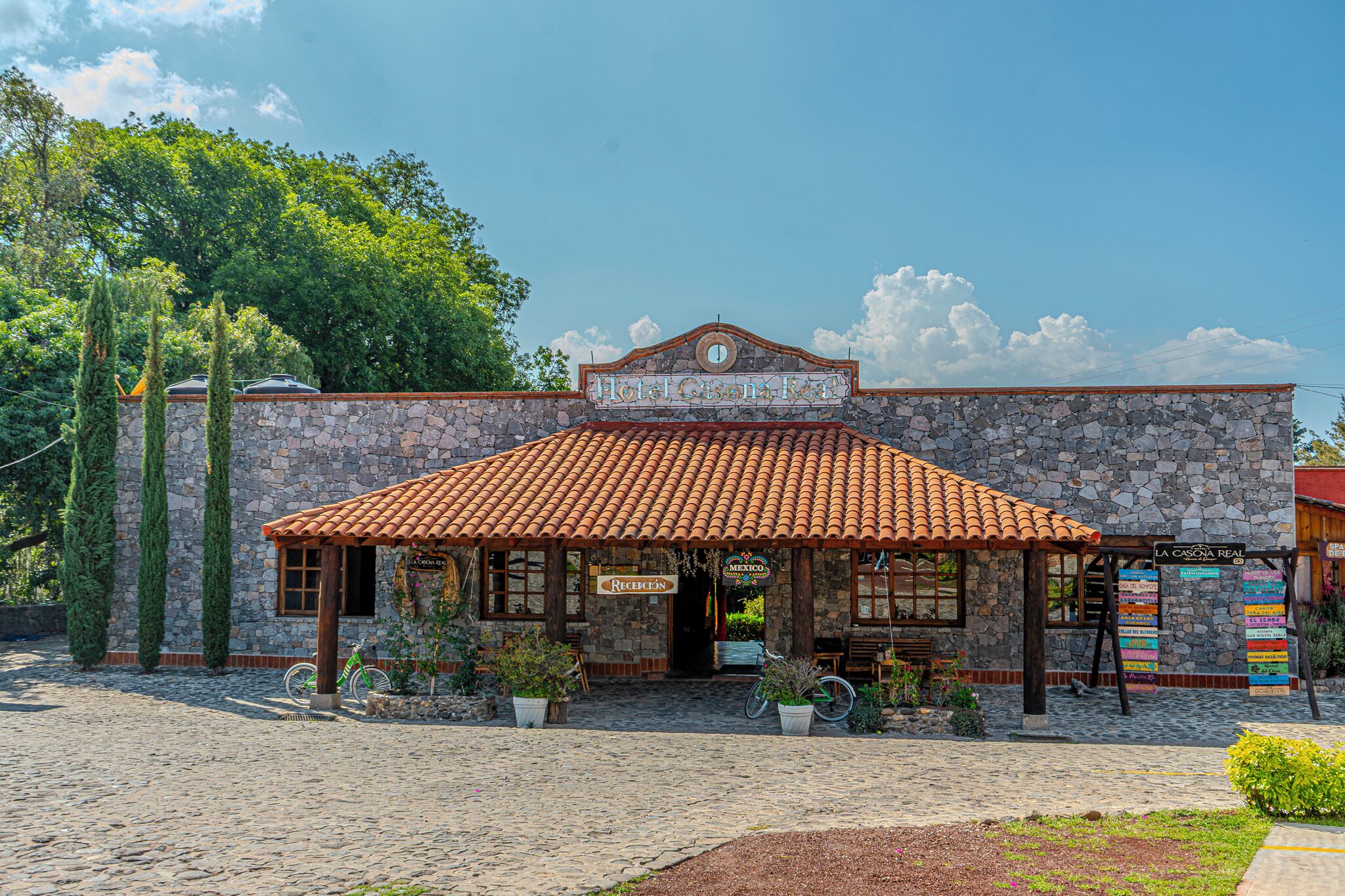 A stone building with a tiled roof, a sign reading 'Hotel Casón Real,' and a sign for 'La Casona Real.'