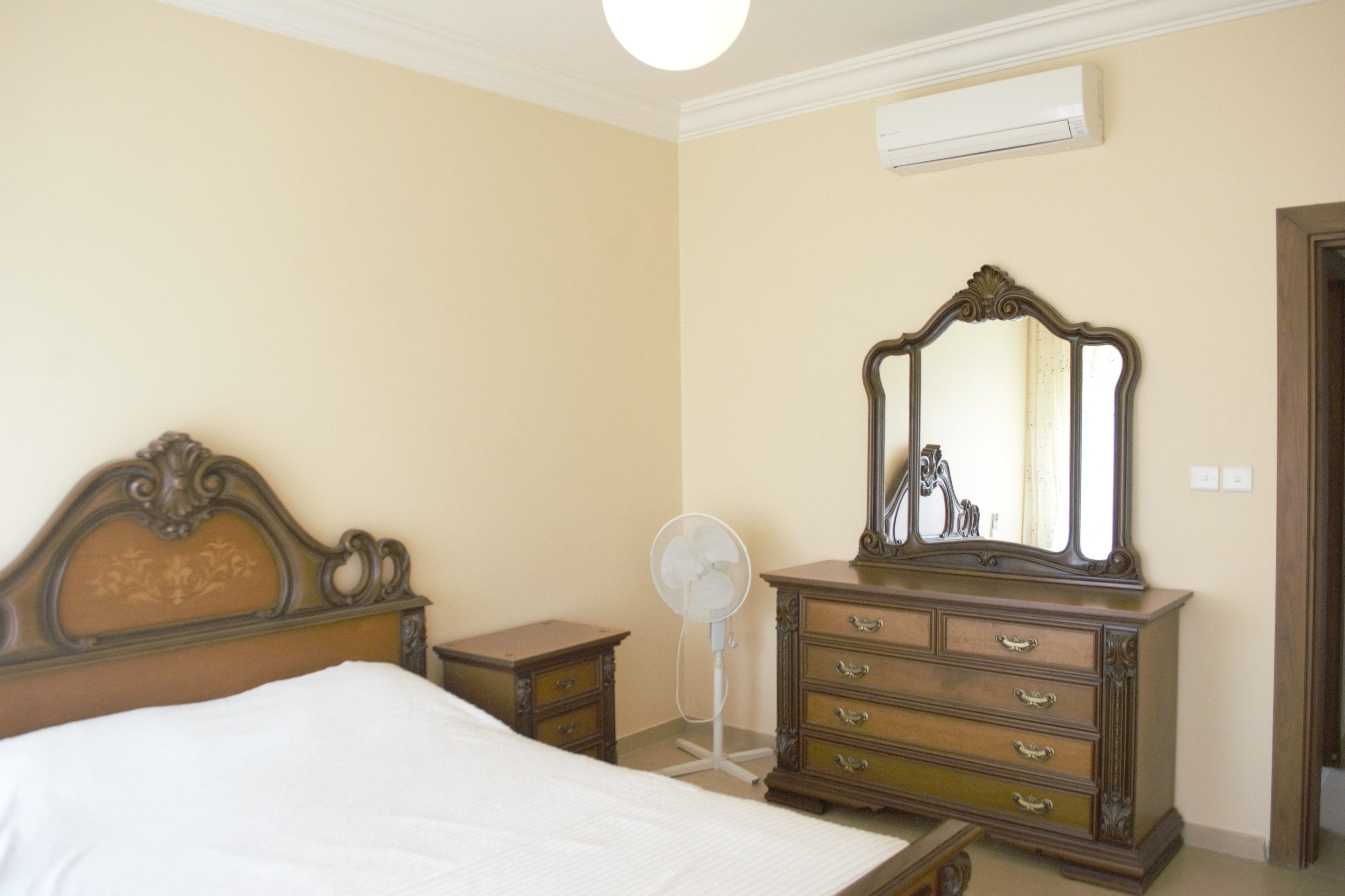 A bedroom with a bed, dresser, mirror, and a standing fan.