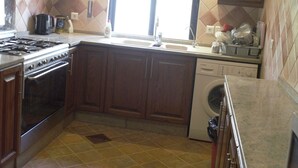 A compact kitchen with a gas stove, oven, dishwasher, and a window providing natural light. - Sports City Jewel (Amman)