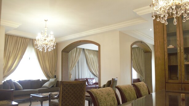 A spacious living room with a chandelier, a sofa set, a dining table, and a wooden cabinet. - Sports City Jewel (Amman)