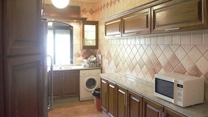A kitchen with a washing machine, microwave, and wooden cabinets. - Sports City Jewel (Amman)