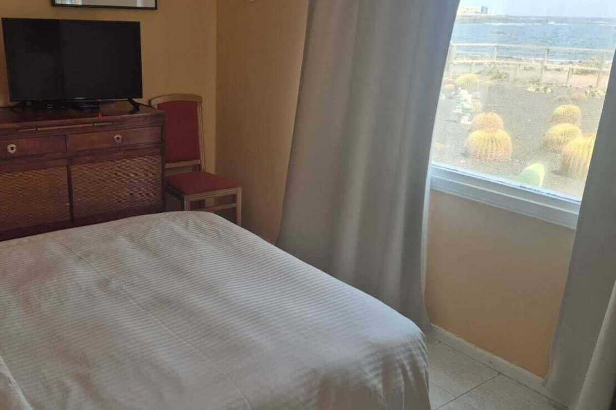 A hotel room with a bed, a dresser, a television, and a view of the beach.