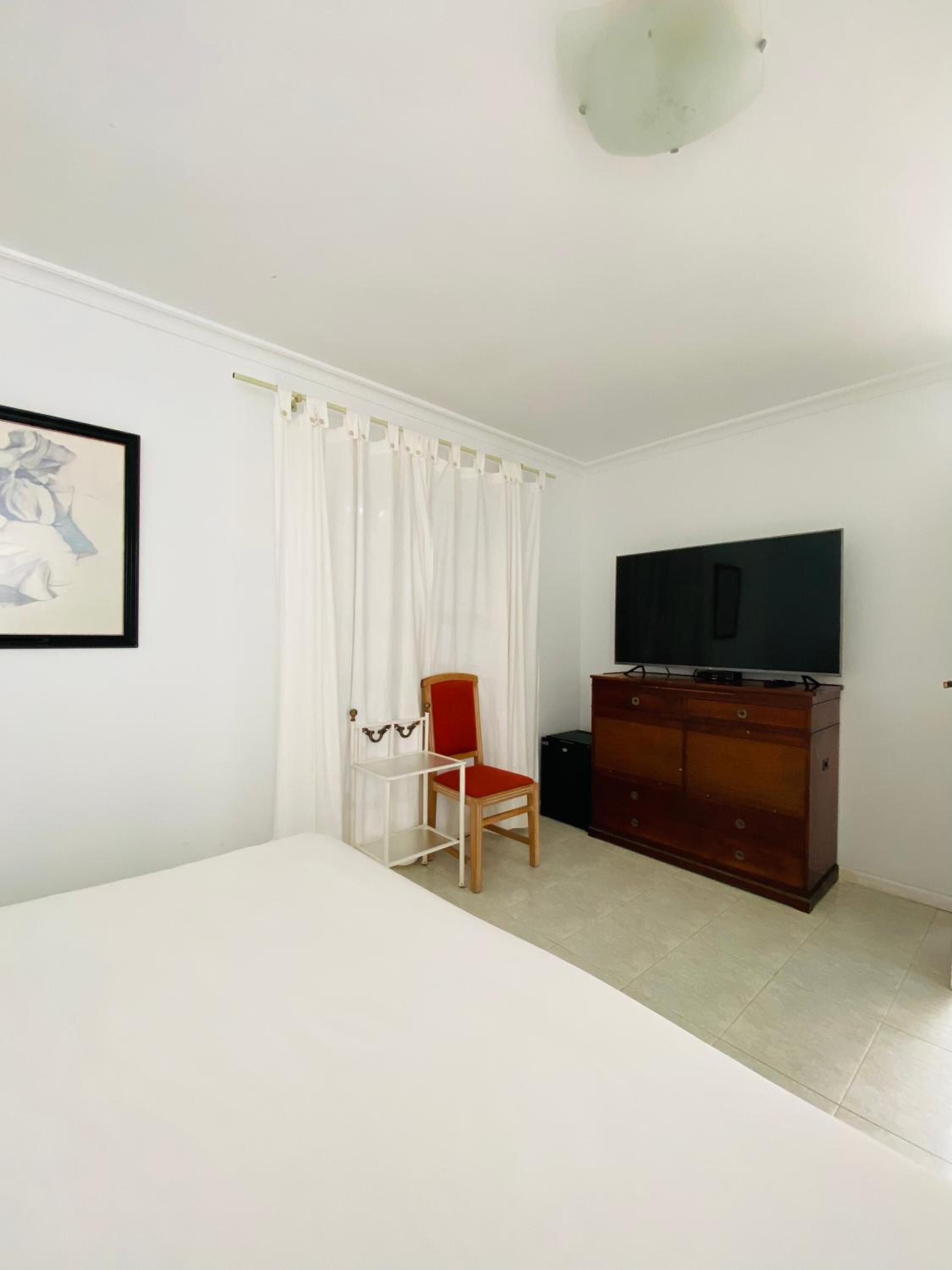 A room with a bed, a chair, a TV, and a dresser.