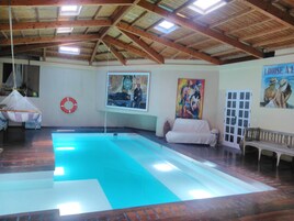 Una piscina interior con techo de madera, una hamaca, un flotador salvavidas y un cuadro en la pared.