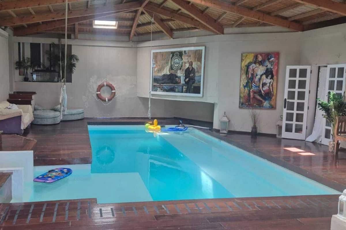 An indoor swimming pool with a wooden deck, a bench, and a lifebuoy on the wall.