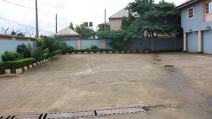 A spacious outdoor area with a concrete floor, surrounded by a low wall with greenery and a building with columns. - Ann's Haven Hotel & Suites (Uyo)