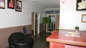A lobby with a black bean bag chair, a wooden table with a menu, framed pictures on the wall, and a potted plant. - Ann's Haven Hotel & Suites (Uyo)