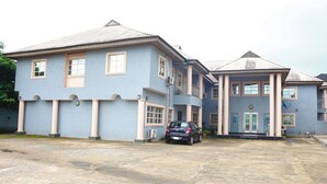 A large, two-story building with a symmetrical facade, featuring a central entrance with a set of stairs leading up to a balcony. - Ann's Haven Hotel & Suites (Uyo)