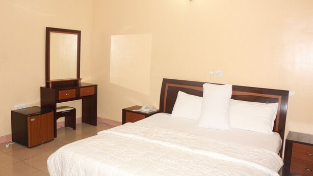 A hotel room with a bed, a dresser, a mirror, and a nightstand with a phone. - Ann's Haven Hotel & Suites (Uyo)