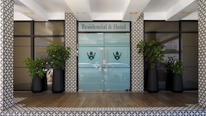Entrada de hotel con puertas dobles, dos macetas a cada lado y suelo con diseño.