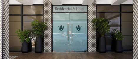 A hotel entrance with a double door, two potted plants on either side, and a patterned floor.