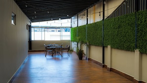Un pasillo con suelo de madera, una mesa con sillas, una planta en maceta y una pared verde con plantas trepadoras.