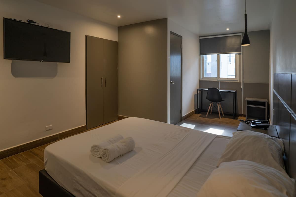 A modern hotel room with a large bed, a desk, and a TV mounted on the wall.