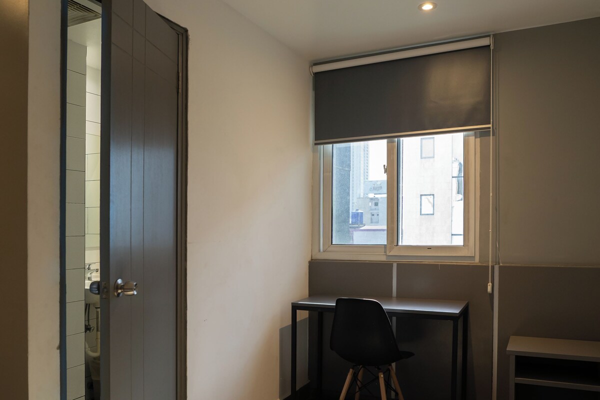 Quarto com escrivaninha, cadeira e janela com persianas.