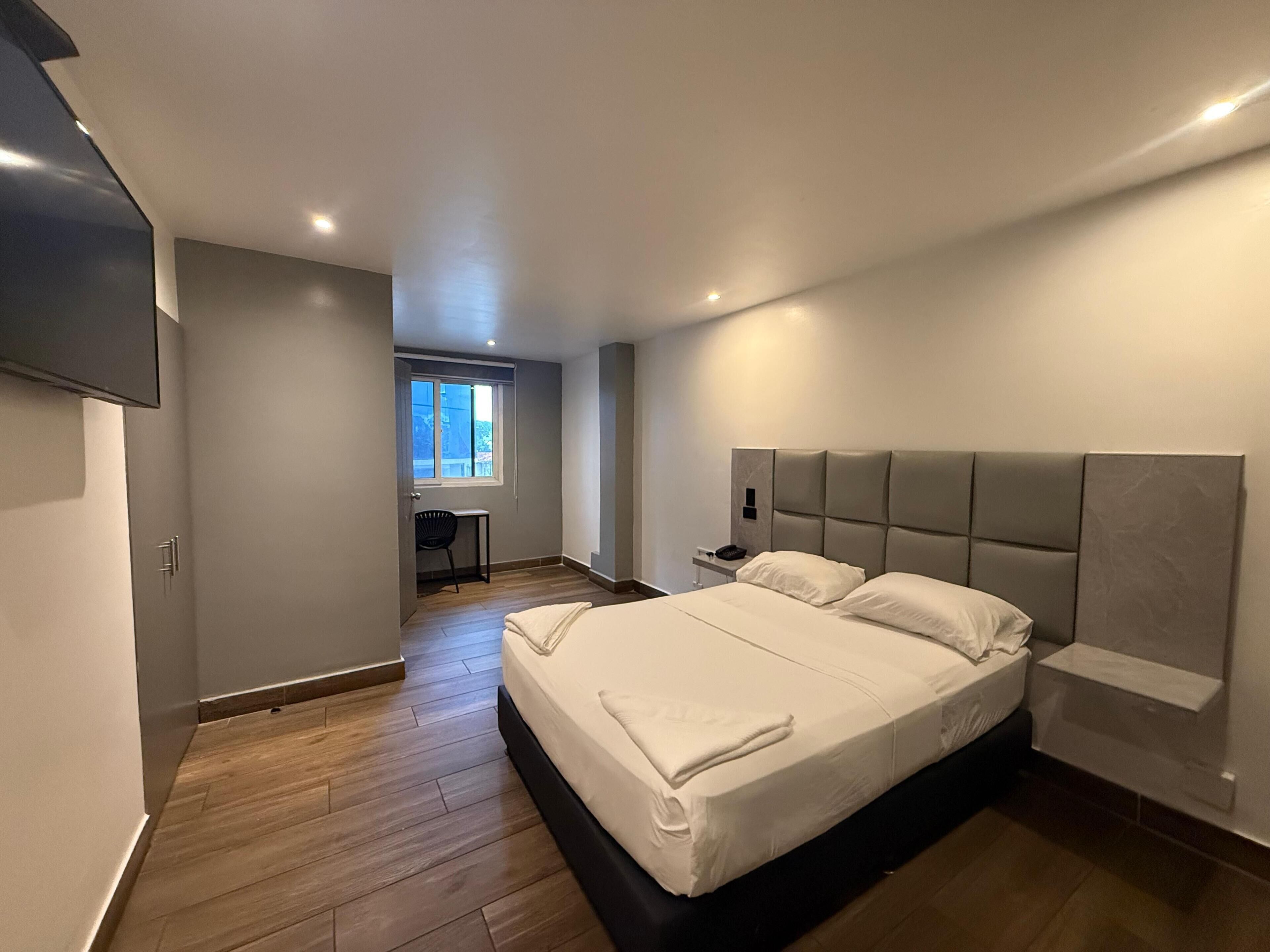 A modern bedroom with a large bed, a desk, and a window.