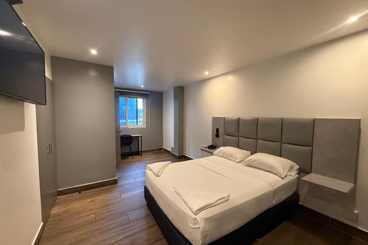 A modern bedroom with a large bed, a desk, and a window.
