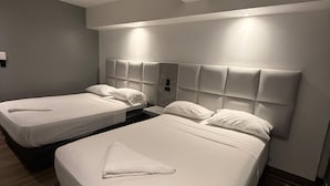 Habitación de hotel con dos camas, cada una con cabecero y ropa de cama blanca.