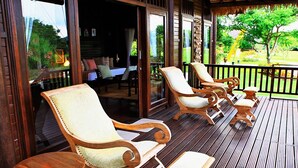 A wooden deck with four lounge chairs and a small table, overlooking a garden. - Samawa Seaside Resort (Sumbawa Besar)