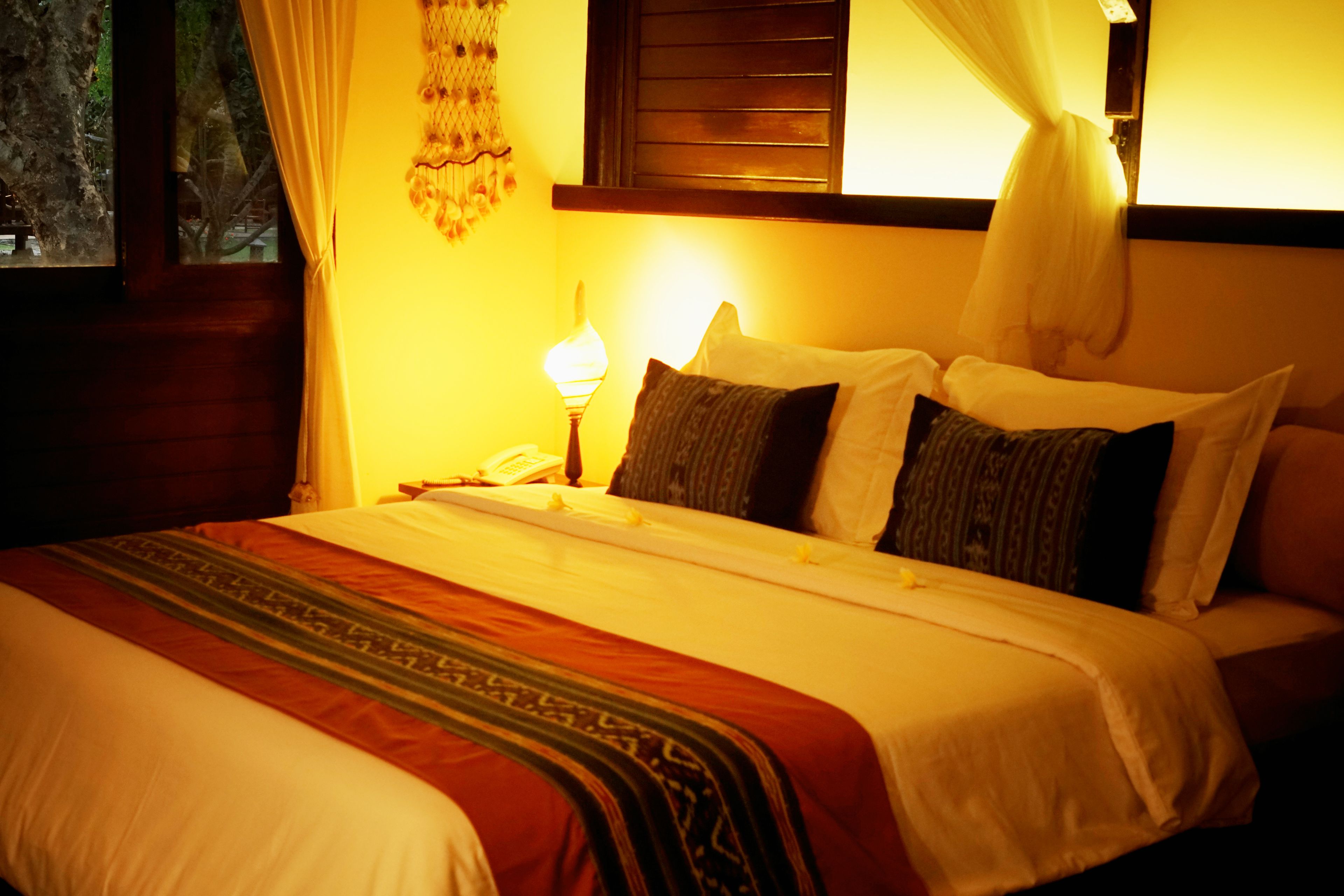 Una cama bien hecha con una colcha estampada, una lámpara de noche y una ventana con cortinas.