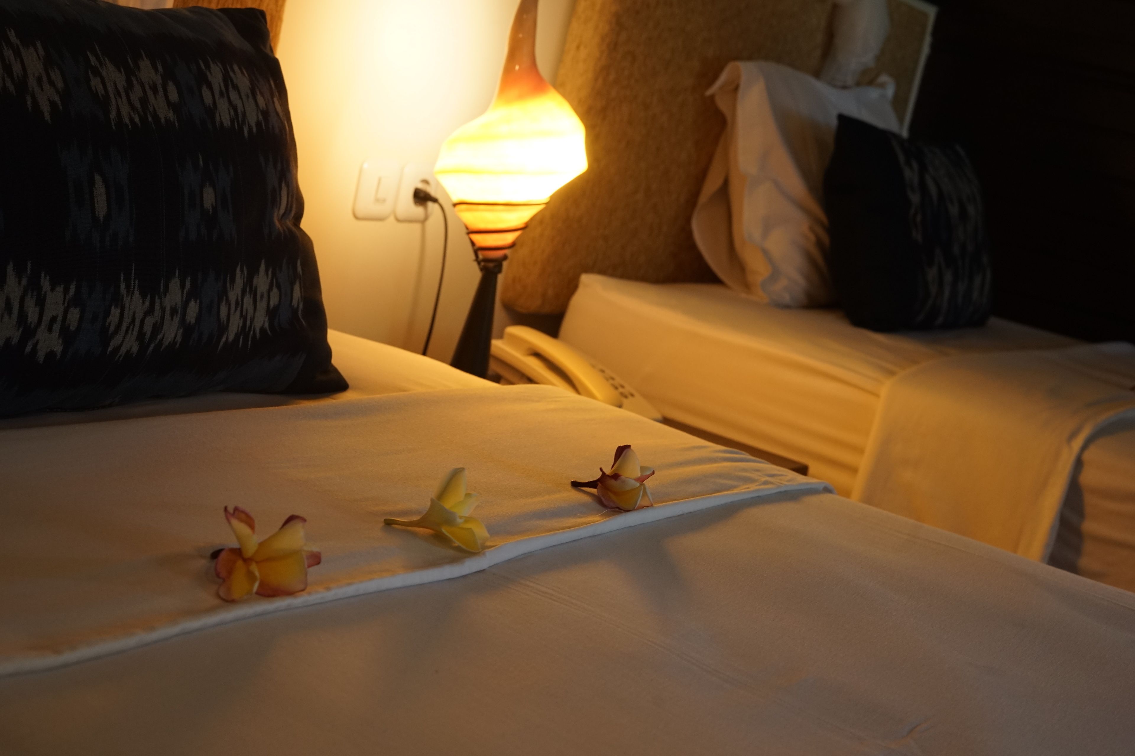 Une chambre d’hôtel avec un lit, des oreillers, une lampe de chevet et quelques fleurs sur le lit.