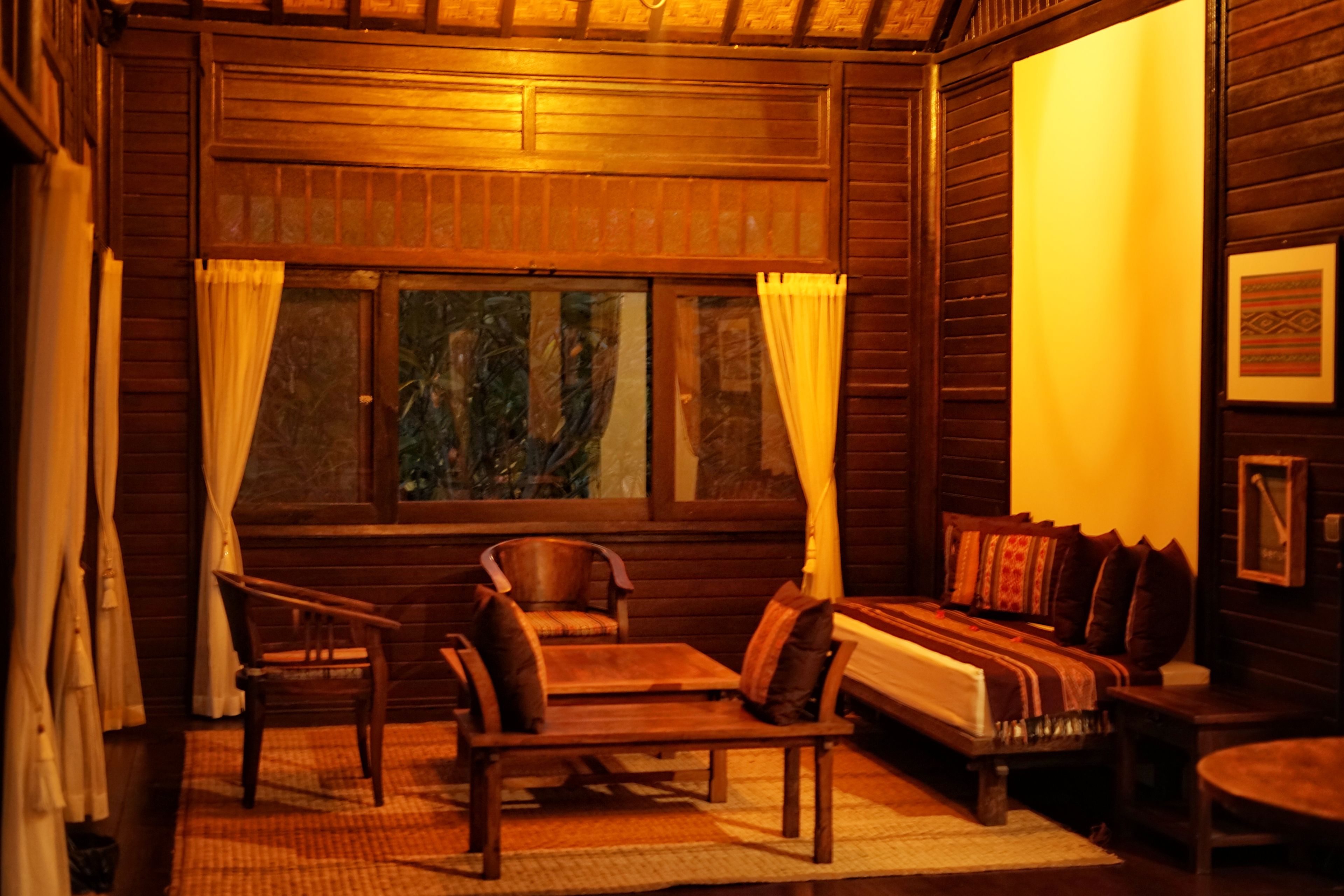 A cozy wooden cabin room with a bed, two chairs, a table, and a window with curtains.