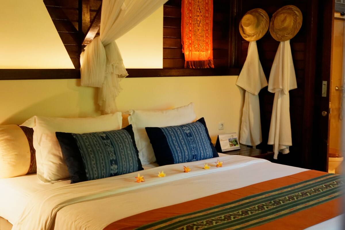 A well-appointed hotel room with a large bed, multiple pillows, a canopy, and a decorative wall hanging.