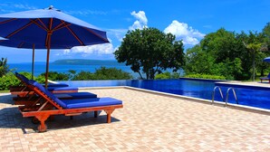 A poolside area with lounge chairs and an umbrella, overlooking a clear blue pool and ocean view. - Samawa Seaside Resort (Sumbawa Besar)