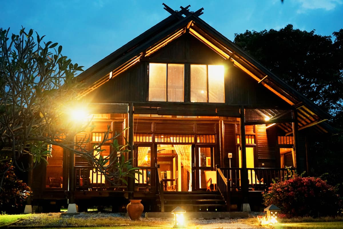 A wooden house with a porch and large windows, surrounded by greenery.