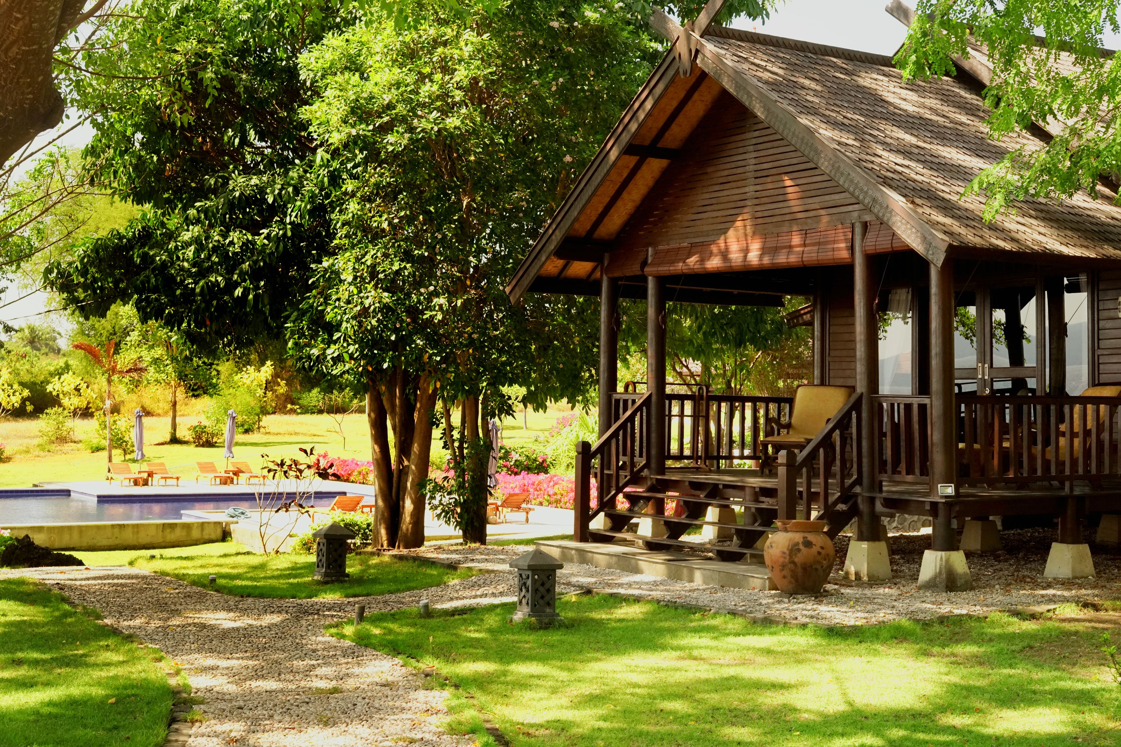 A wooden gazebo with a covered porch, surrounded by lush greenery and a swimming pool.