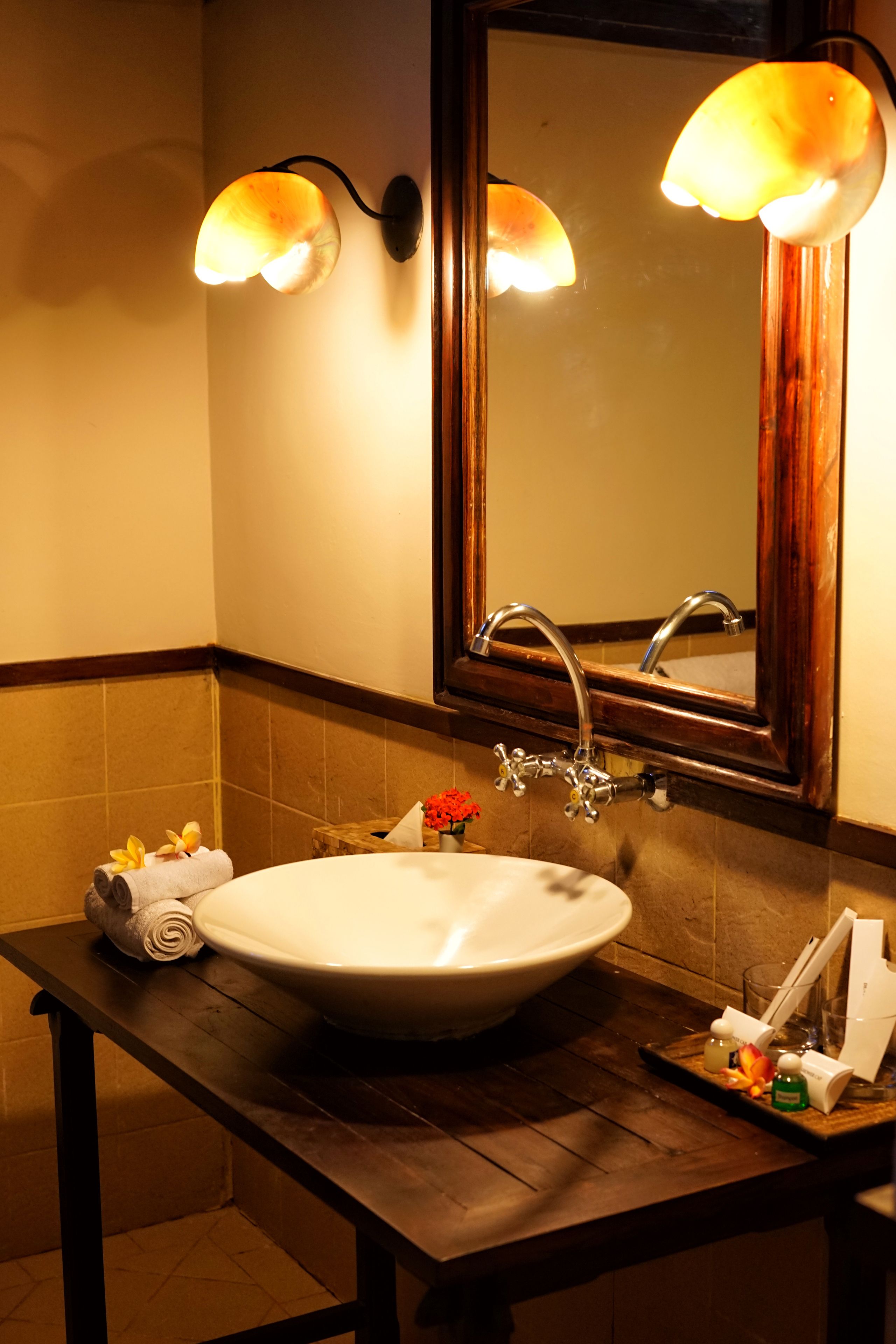 Une salle de bain avec un grand lavabo blanc, deux lampes fixées au mur, un meuble-lavabo en bois et un miroir avec un cadre en bois.