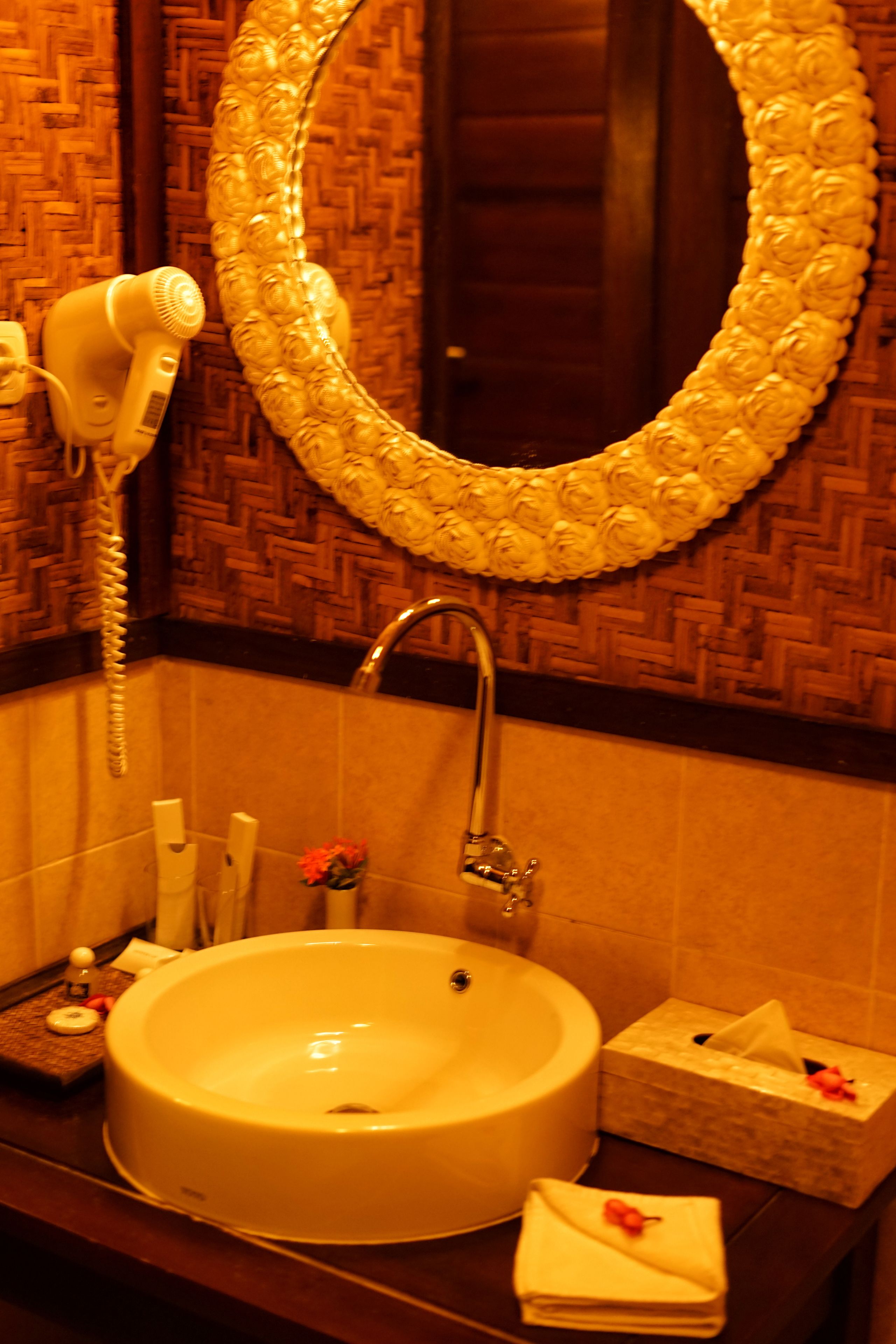 Un baño con un lavamanos redondo, un espejo con marco floral, un secador de pelo y un armario para toallas.