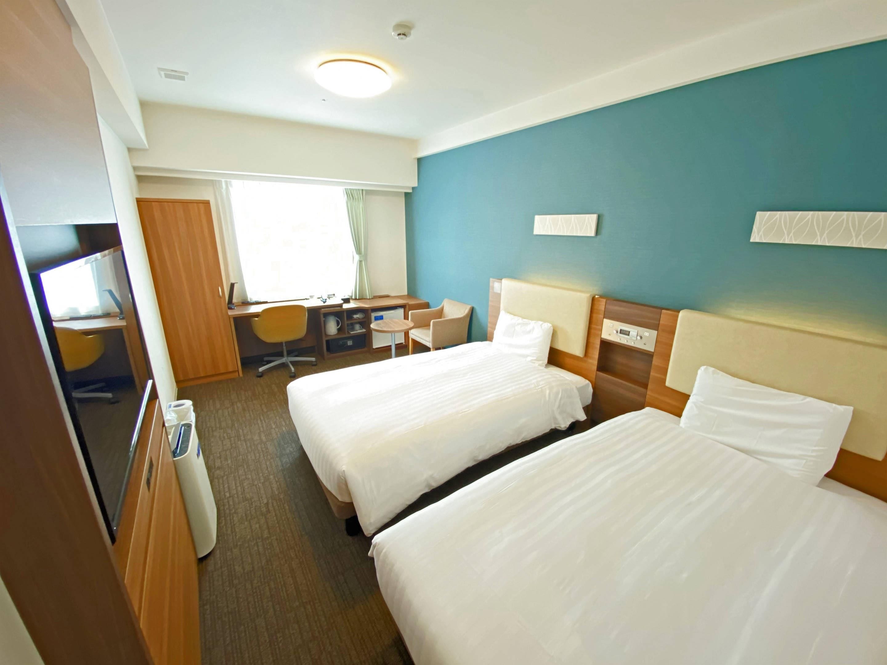 A hotel room with two beds, a desk, a chair, and a small table.