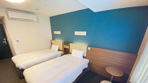 A hotel room with two single beds, a small round table, and a wall-mounted air conditioner.