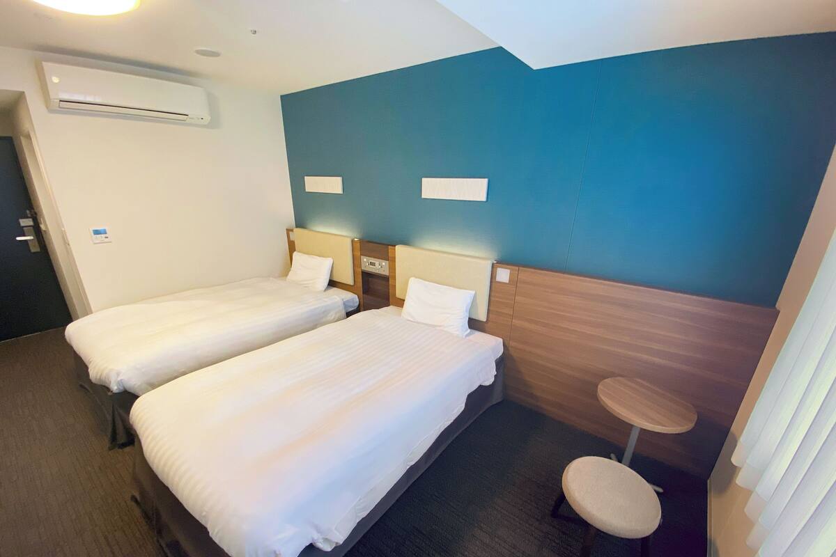 Habitació d'hotel amb dos llits individuals, una taula rodona petita i un aire condicionat fixat a la paret.