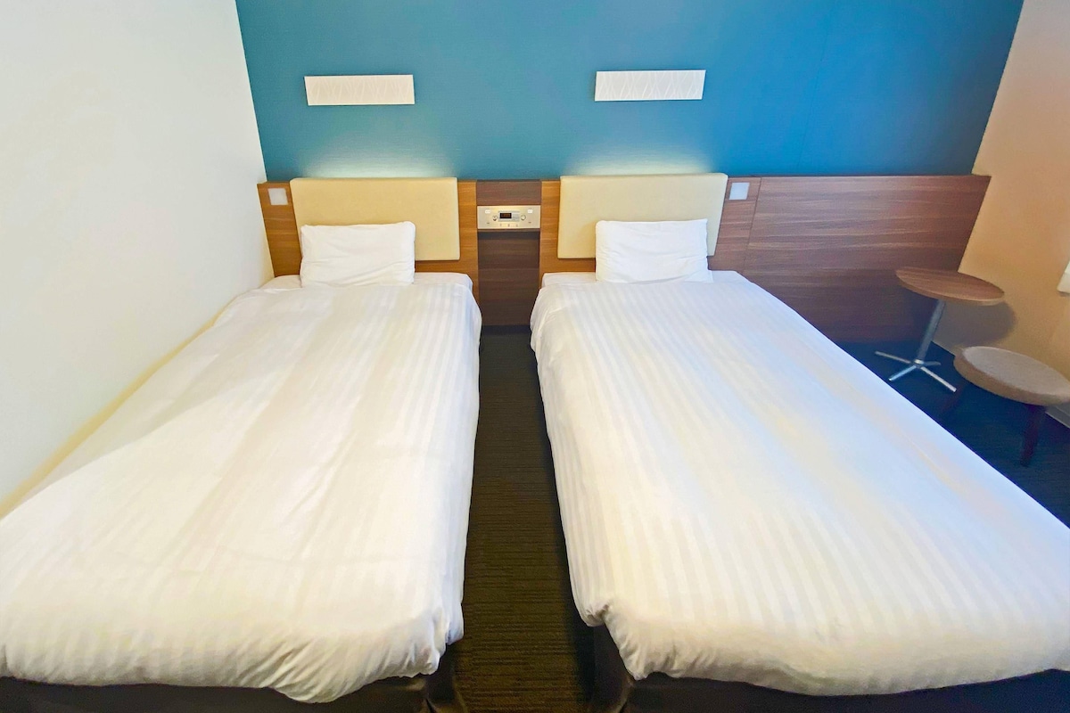 Ein Hotelzimmer mit zwei Einzelbetten, einem kleinen runden Tisch und einer an der Wand montierten Steuerung.