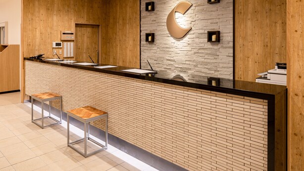 A reception desk with a wooden finish, a stone wall with a crescent moon design, and two metal stools.