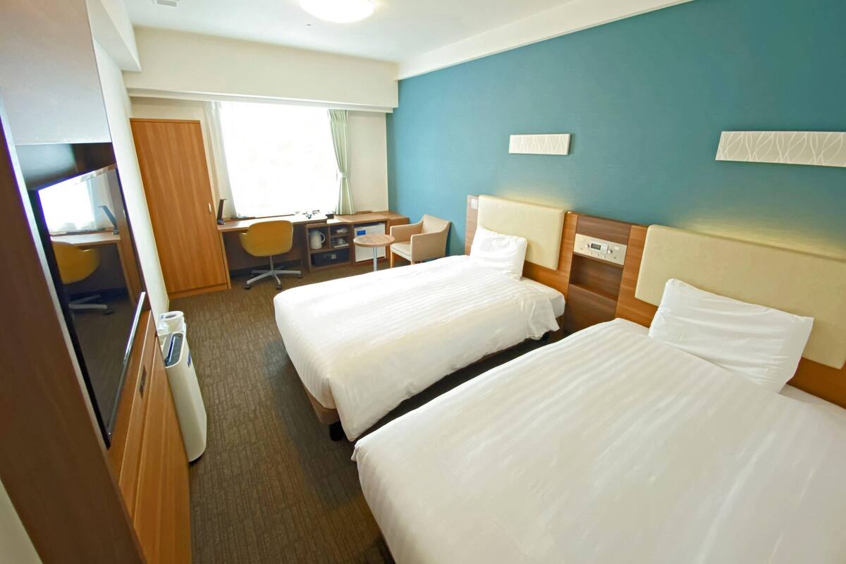 Habitació d'hotel amb dos llits, una escriptori, una cadira i una taula petita.