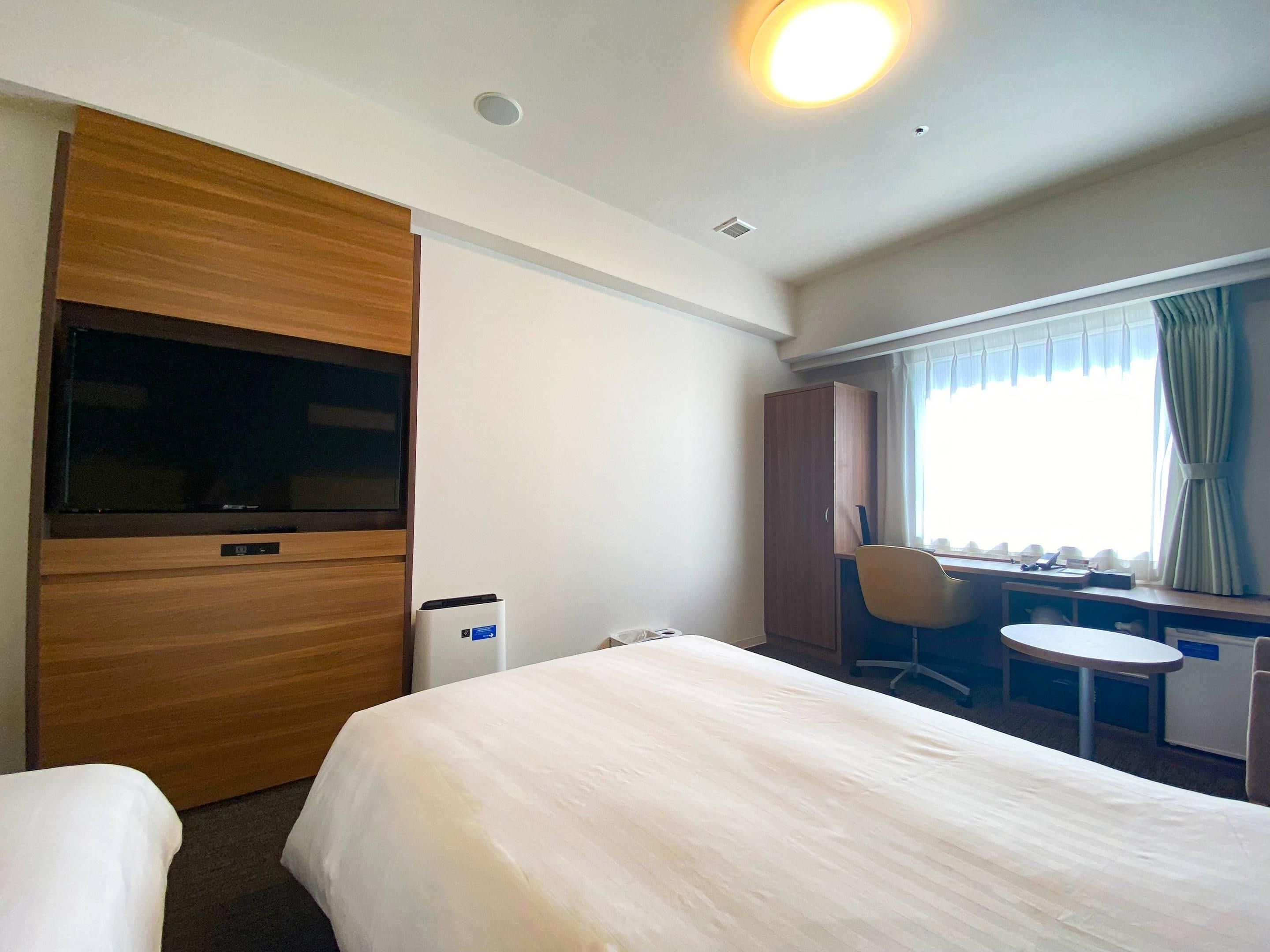 A hotel room with a bed, a desk, a chair, a wardrobe, and a television.