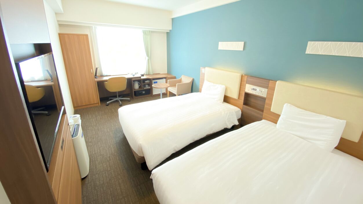 A hotel room with two beds, a desk with a chair, a TV, and a small table.