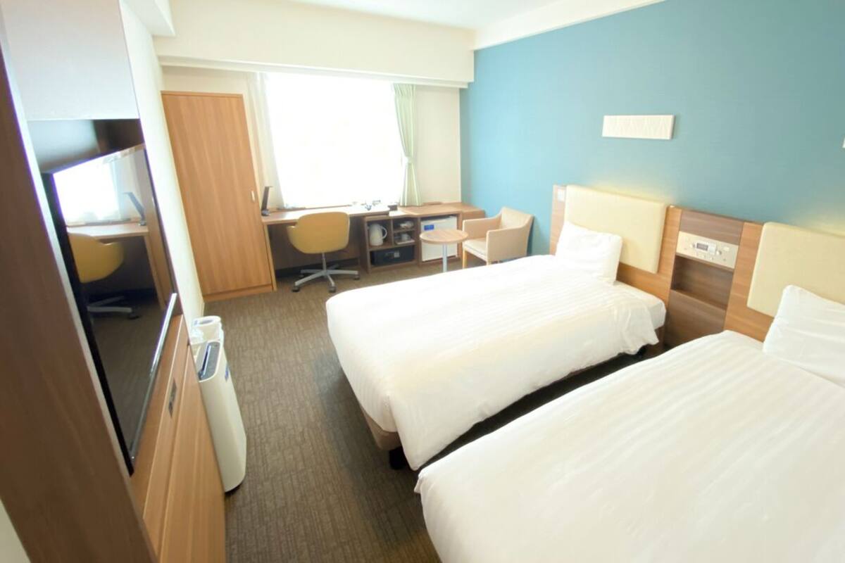 Una habitació d'hotel amb dos llits, una escriptori amb una cadira, una televisió i una taula petita.