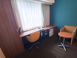 Una habitación de hotel con un escritorio de madera, una silla, una mesita pequeña y un armario.