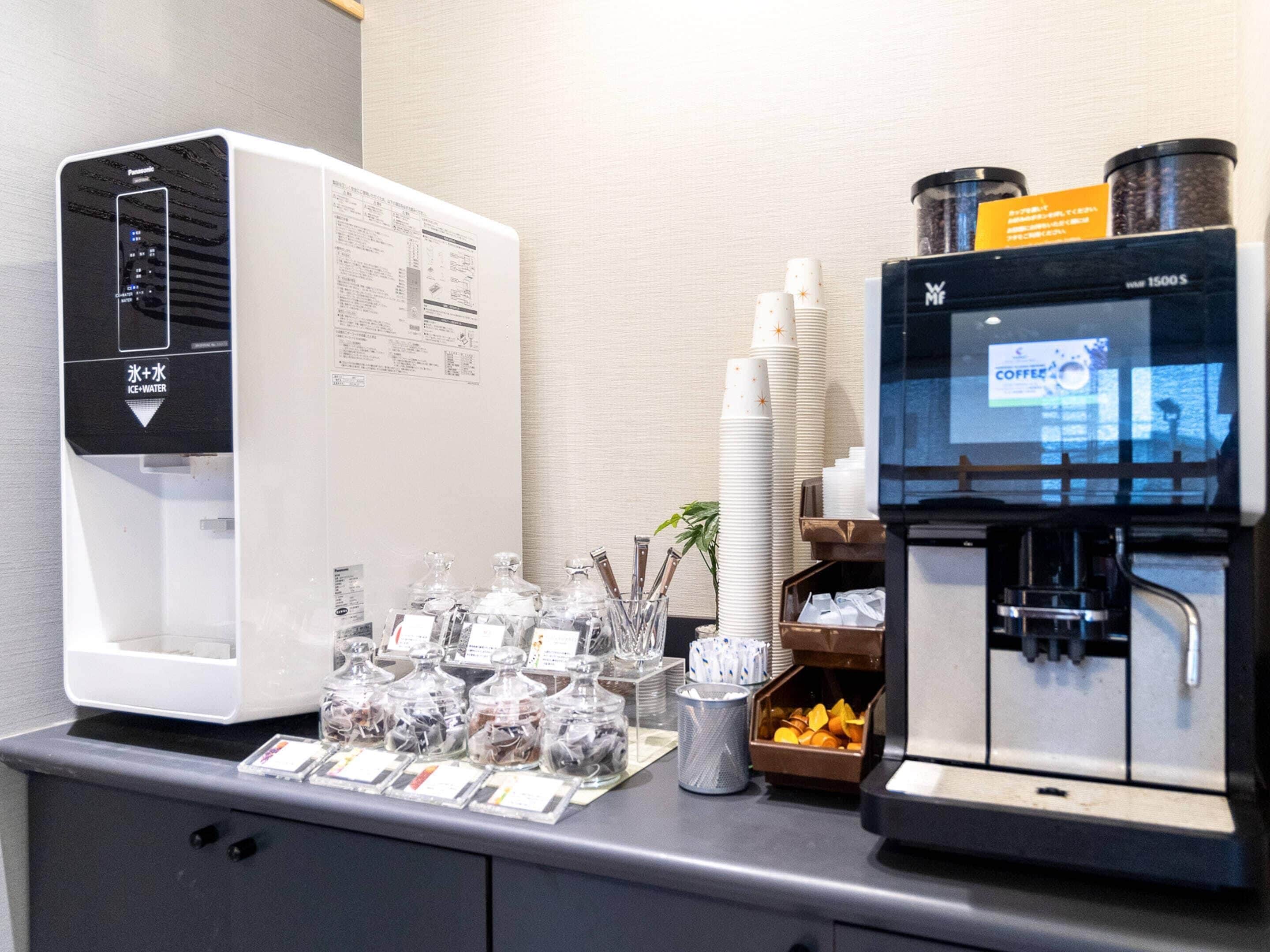 A coffee station with a coffee machine, a water dispenser, and a display of coffee cups and sugar packets.