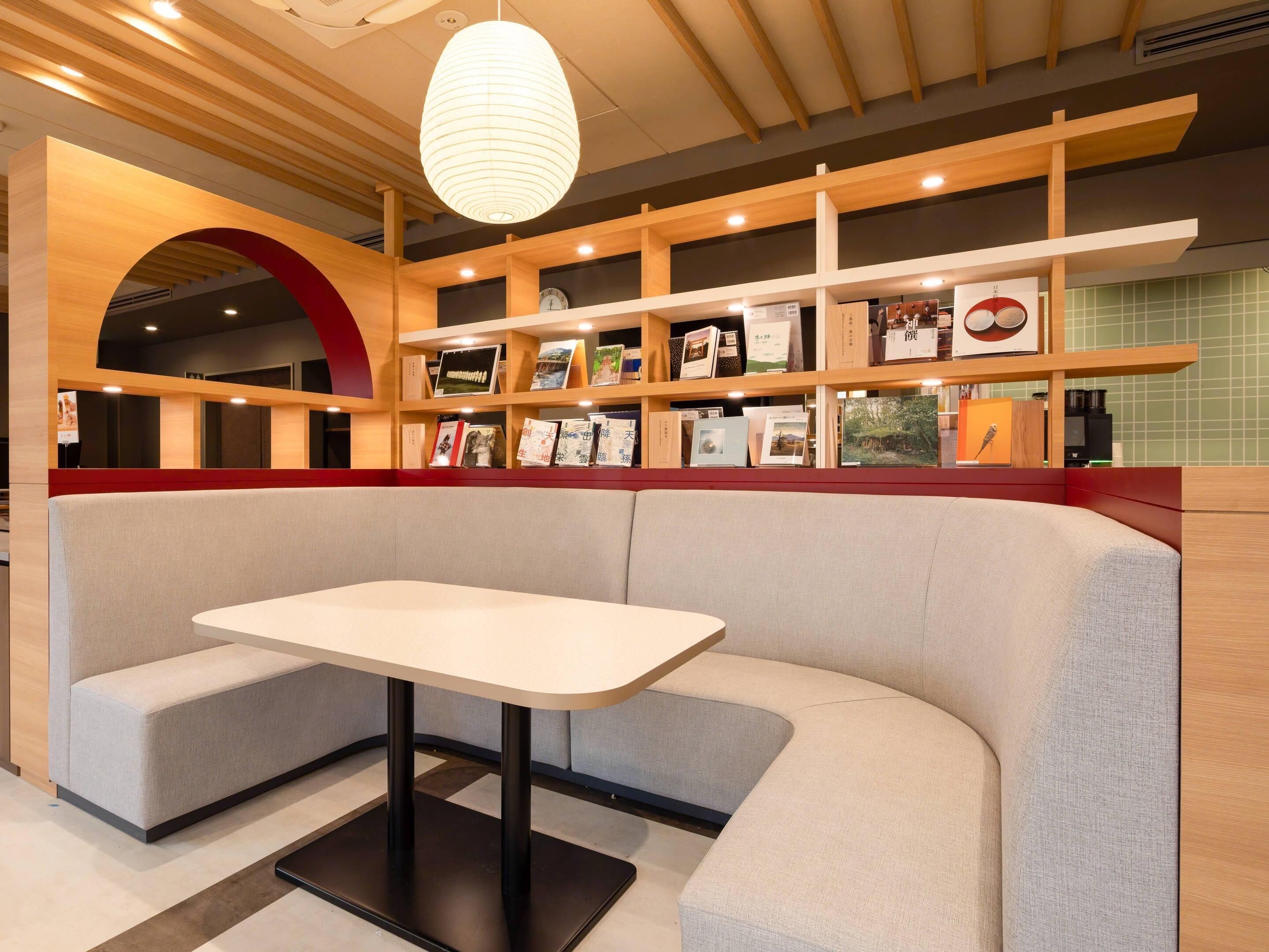 A modern interior with a booth seating area, wooden shelves with books, and a hanging light fixture.