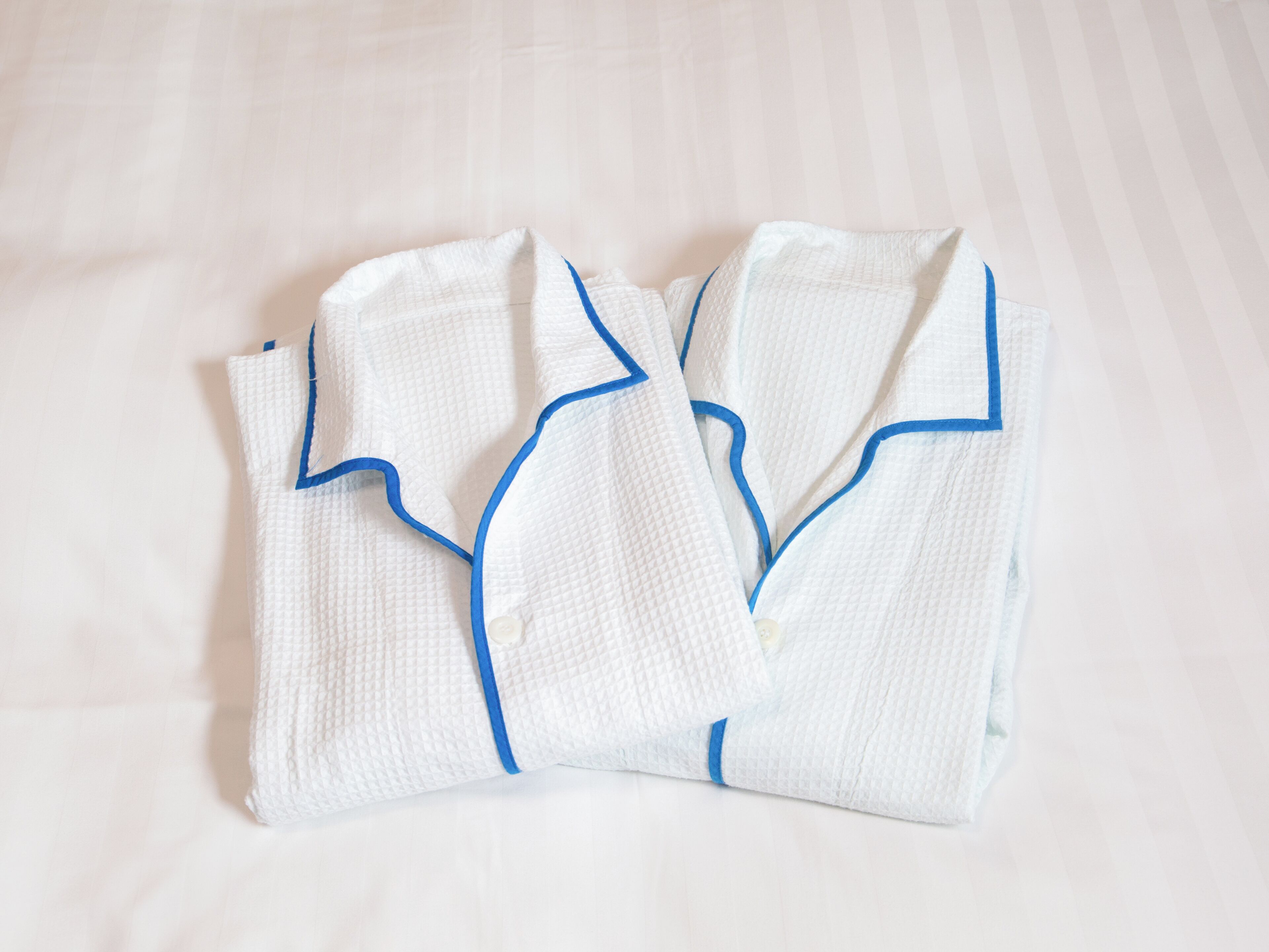 Neatly folded white robes with blue trim on a bed.