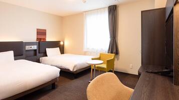 A hotel room with two beds, a small table, a chair, a TV, and a window with curtains.