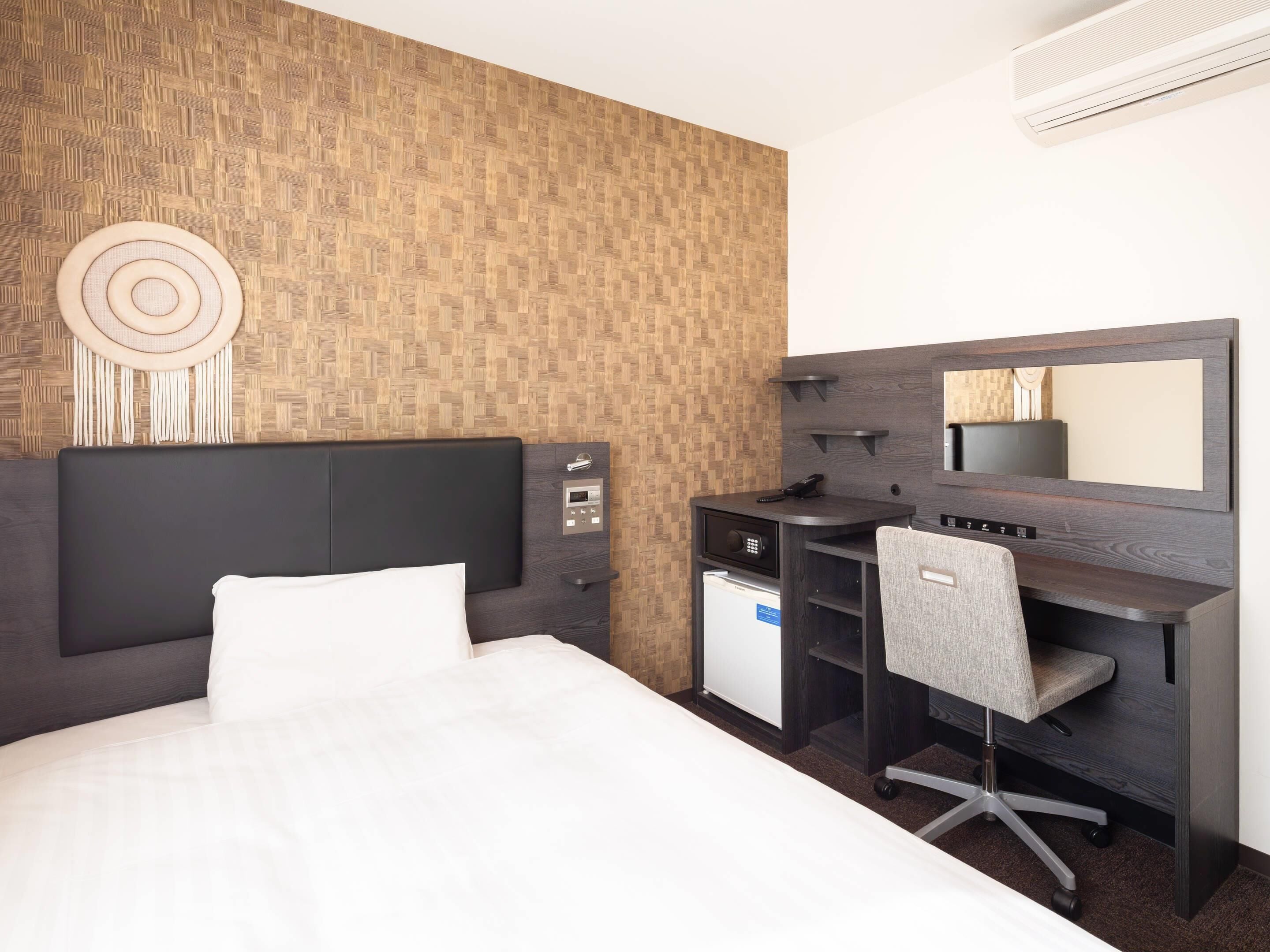Habitación de hotel con cama, escritorio y silla, refrigerador pequeño, espejo y aire acondicionado instalado en la pared.