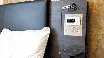 Una habitación moderna con cama, un reloj digital y un panel de control con botones para los pies, lectura y la habitación.