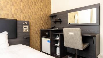 A hotel room with a bed, a desk, a chair, a small refrigerator, a microwave, a coffee maker, a telephone, a control panel, and a mirror.